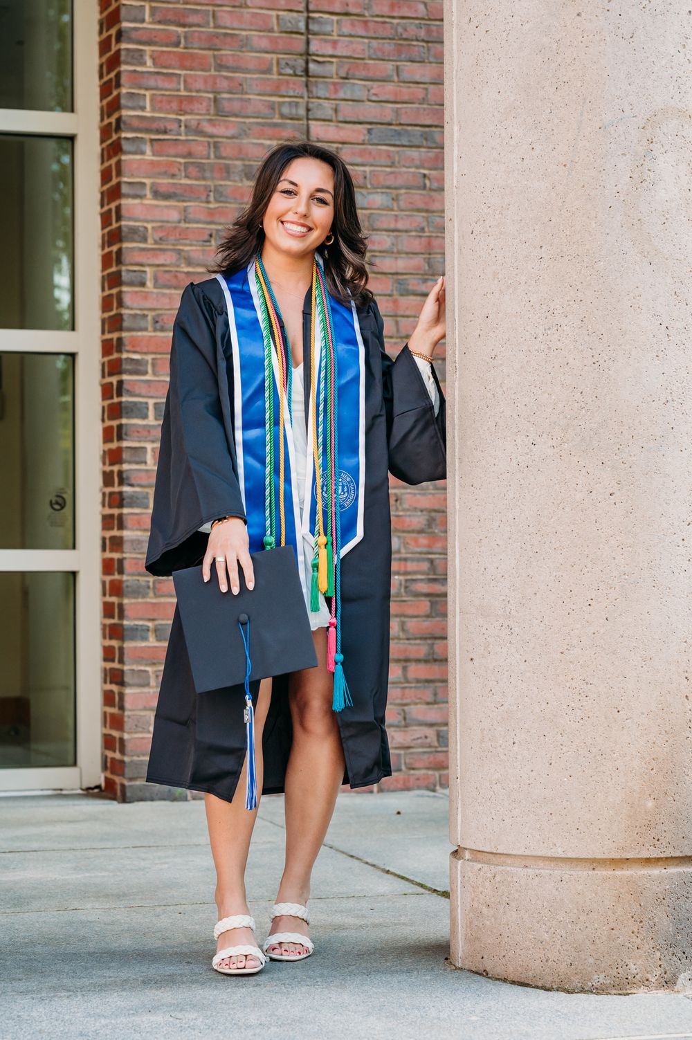 Graduation photo series showing a graduate in cap and gown with decorative stole posing in various angles near brick building.