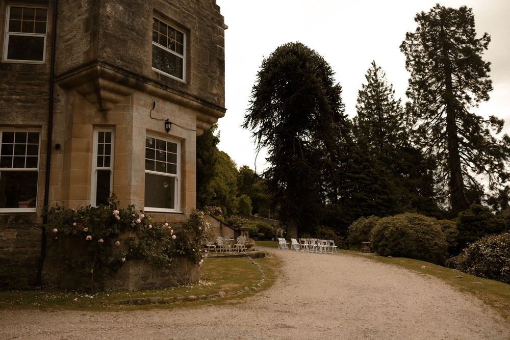Stone mansion building facade with multiple windows and architectural details against a cloudy sky and surrounding trees.