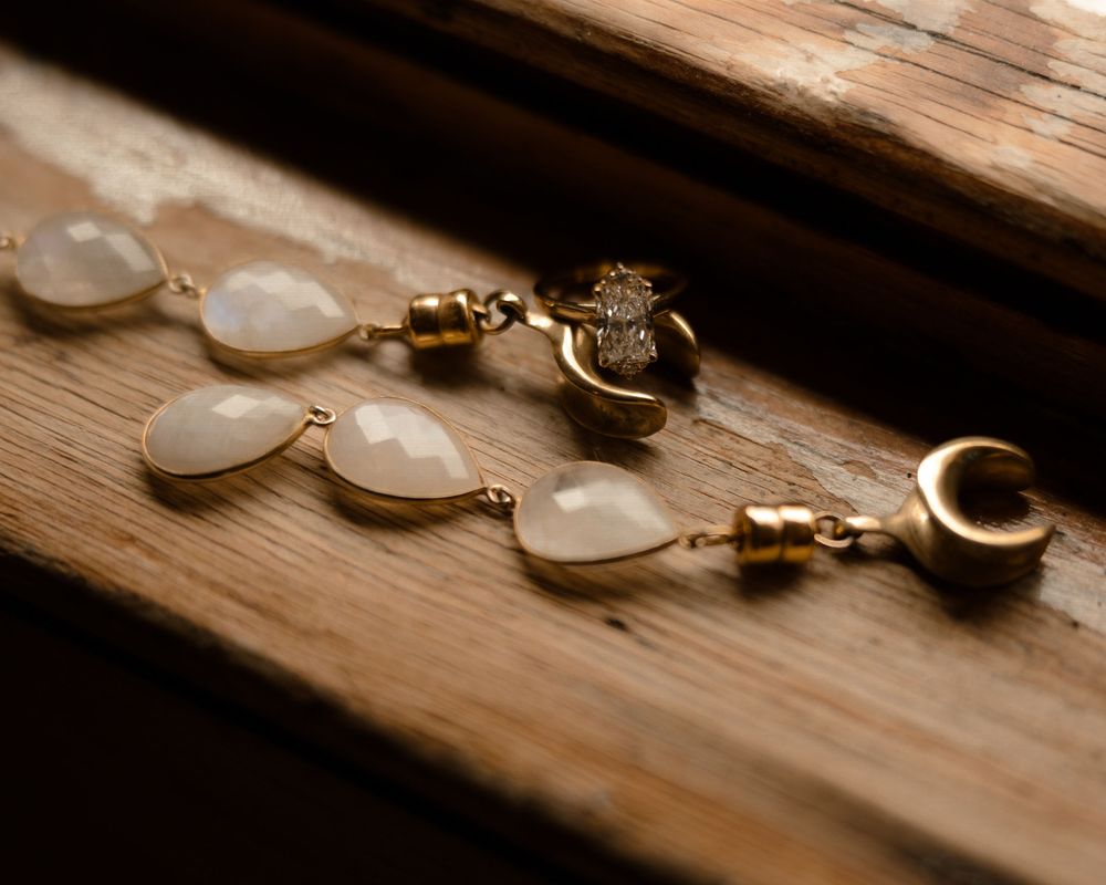 Delicate moonstone teardrop earrings with celestial charms laid on rustic wooden surface in warm lighting.