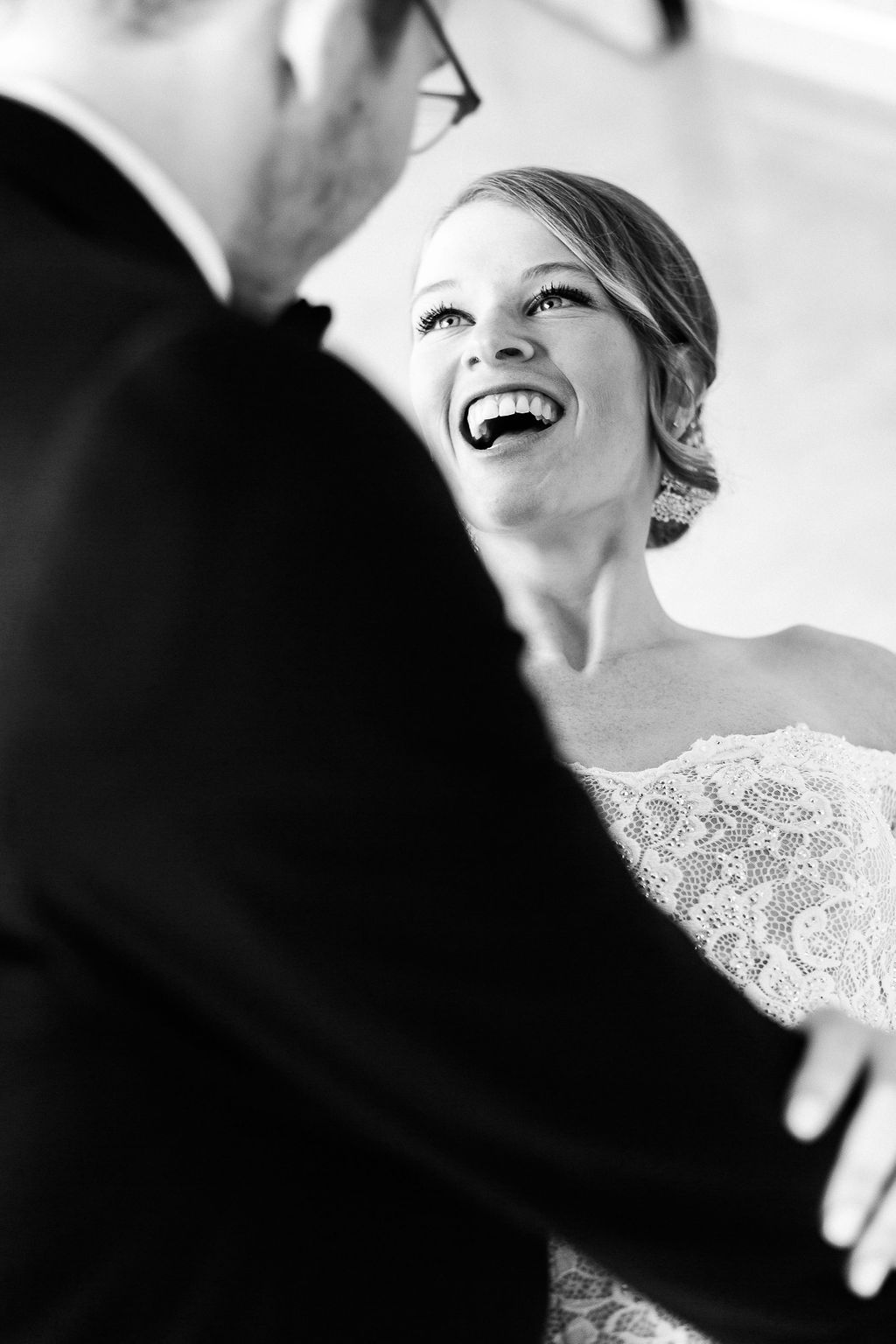 Black and white photo of a bride in lace dress laughing joyfully during an intimate wedding moment.