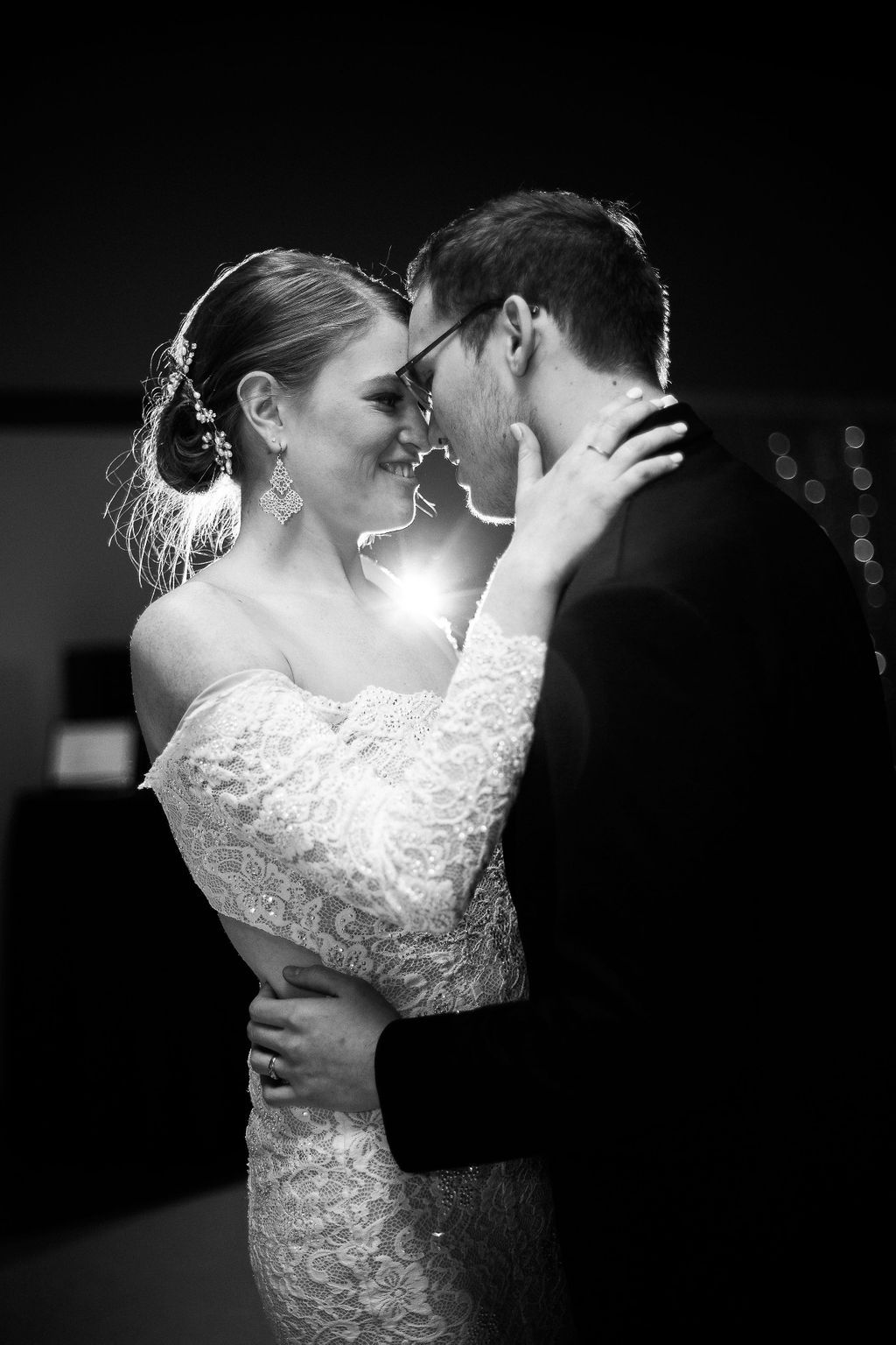 Romantic black and white portrait of newlyweds embracing during their first dance in soft lighting.