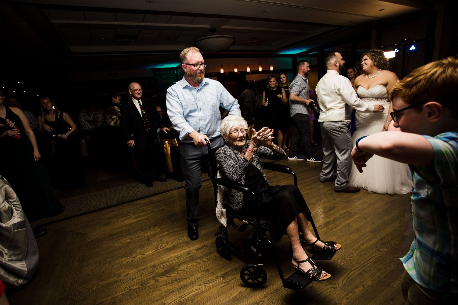 A person pushes someone in a wheelchair across a dance floor during what appears to be a lively celebration.