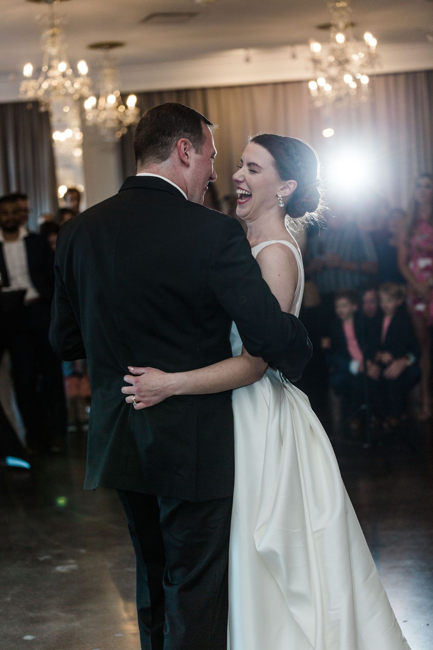 A couple shares a joyful moment during their first dance at a wedding reception under sparkling chandeliers.