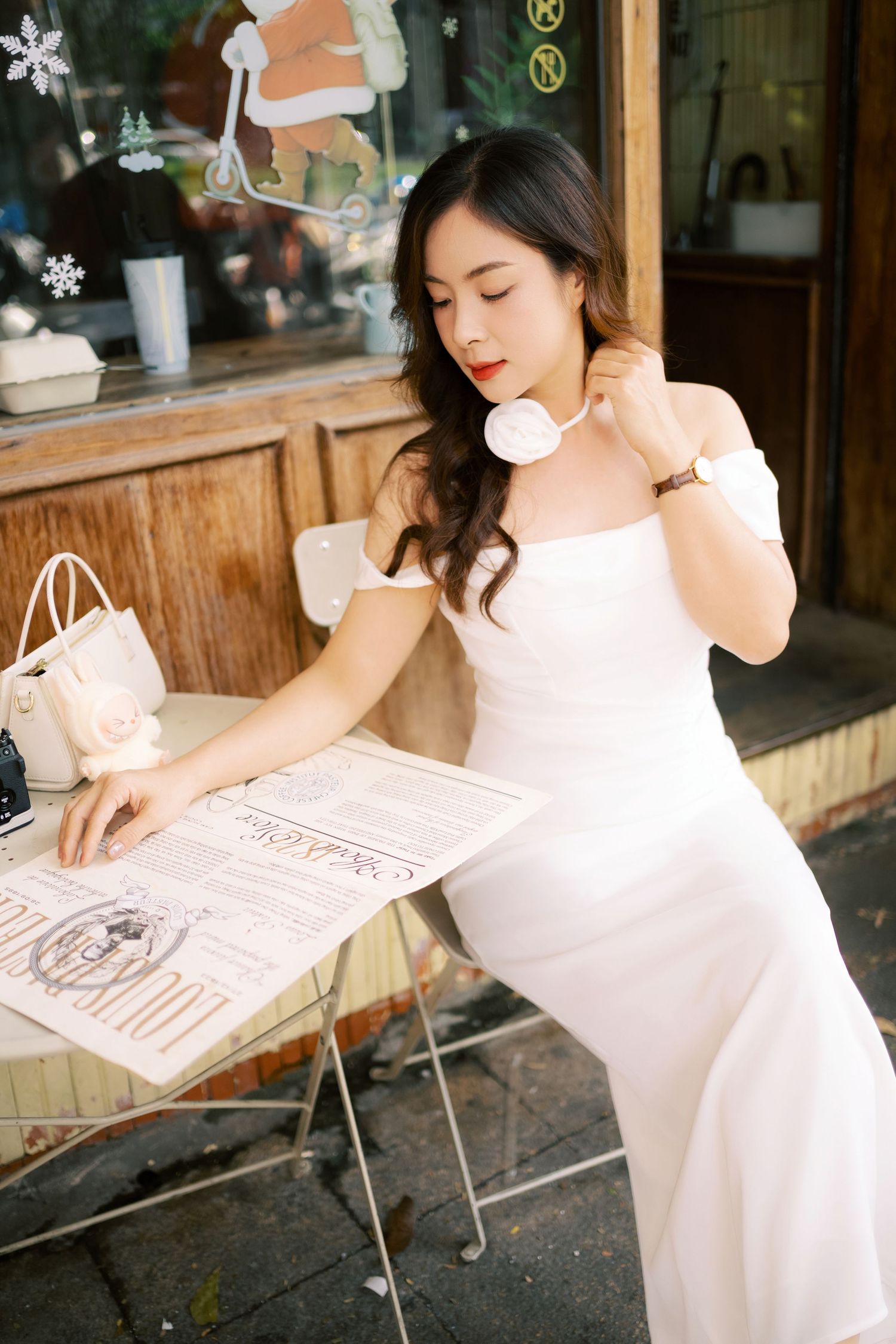 Someone in a flowing white dress writes on a menu board at an outdoor cafe on a sunny day.