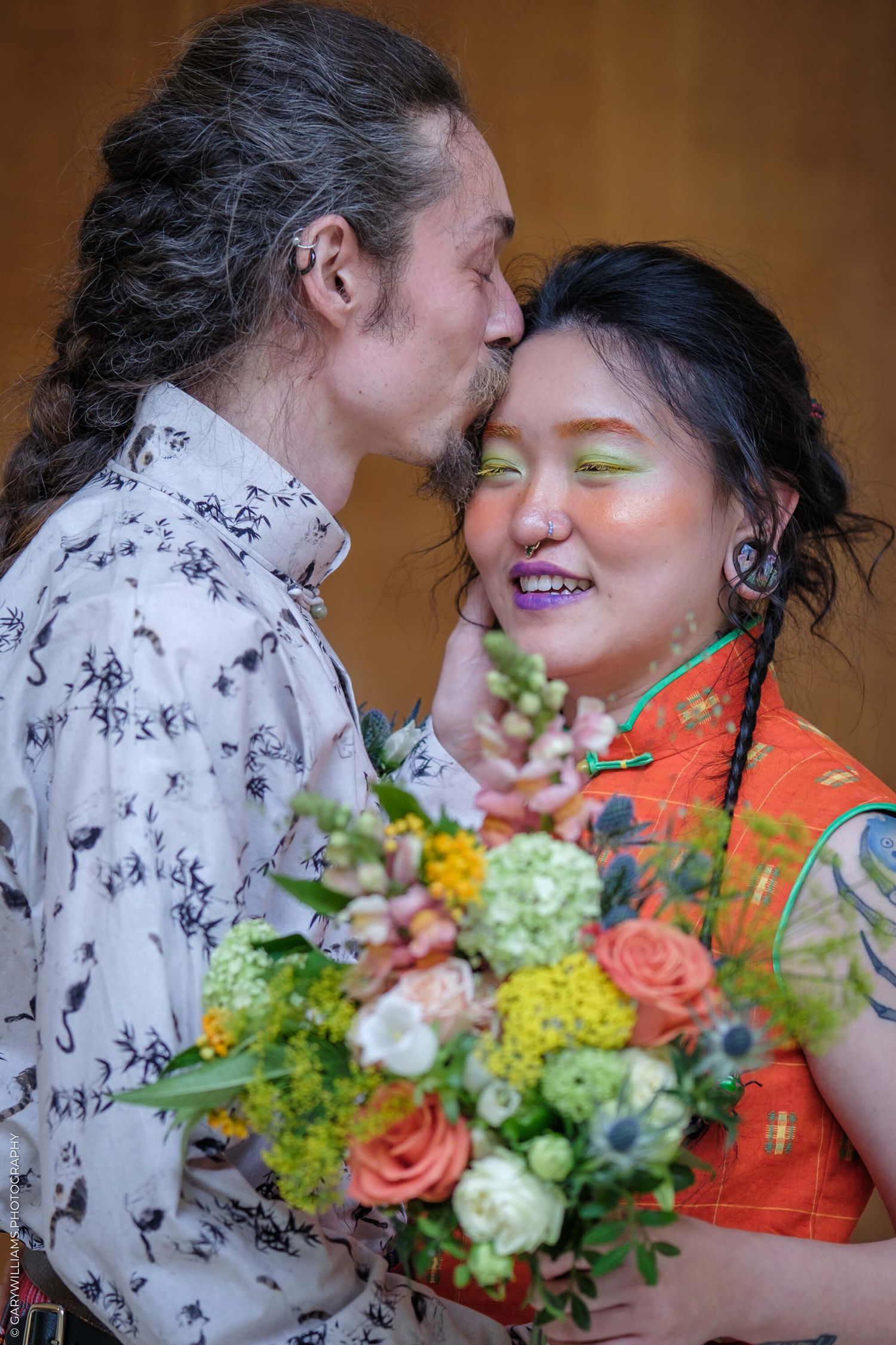 A tender intimate moment captured with a beautiful floral bouquet featuring roses and greenery against warm lighting.