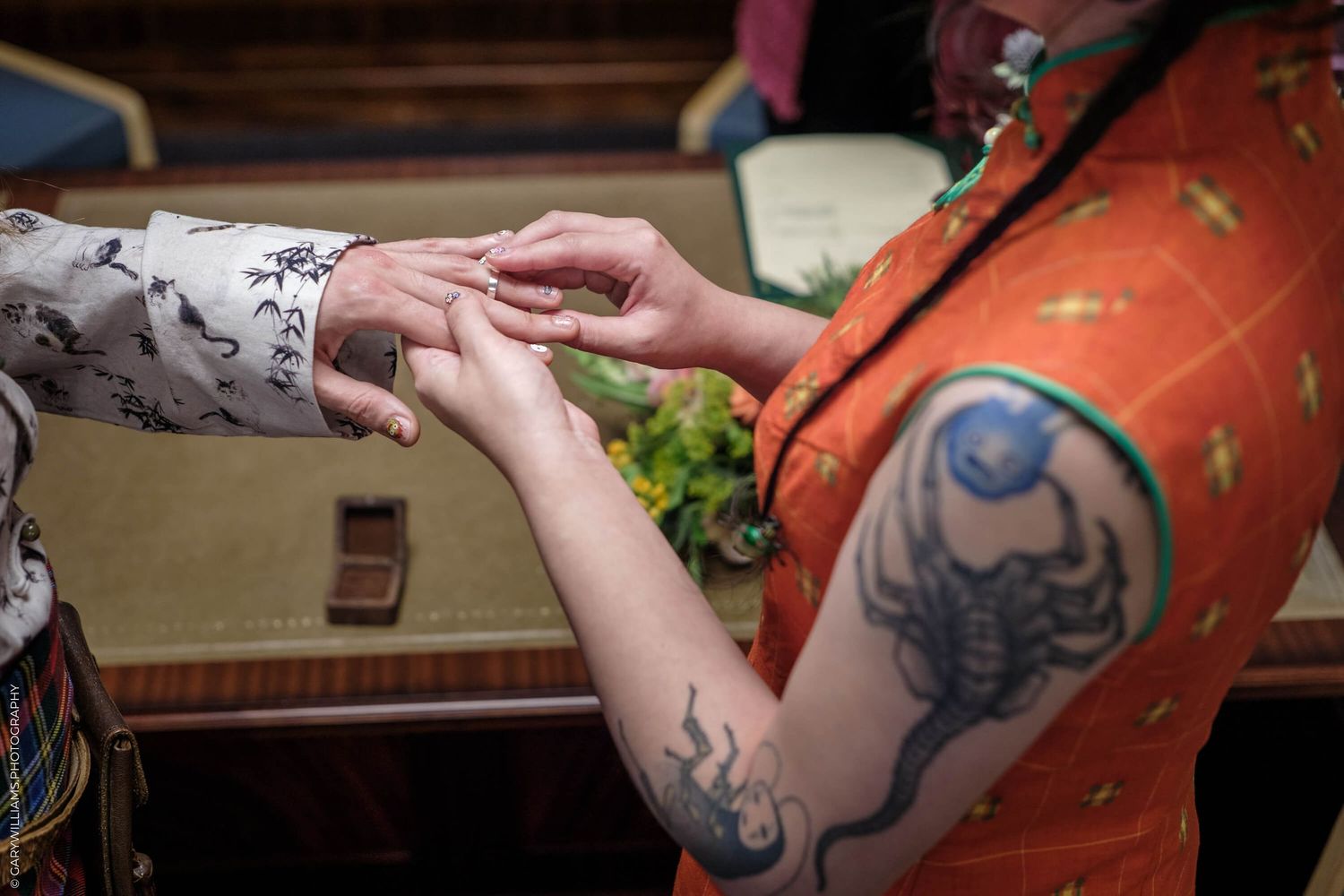 Two tattooed hands reach towards each other in a close encounter during a quiet indoor moment.