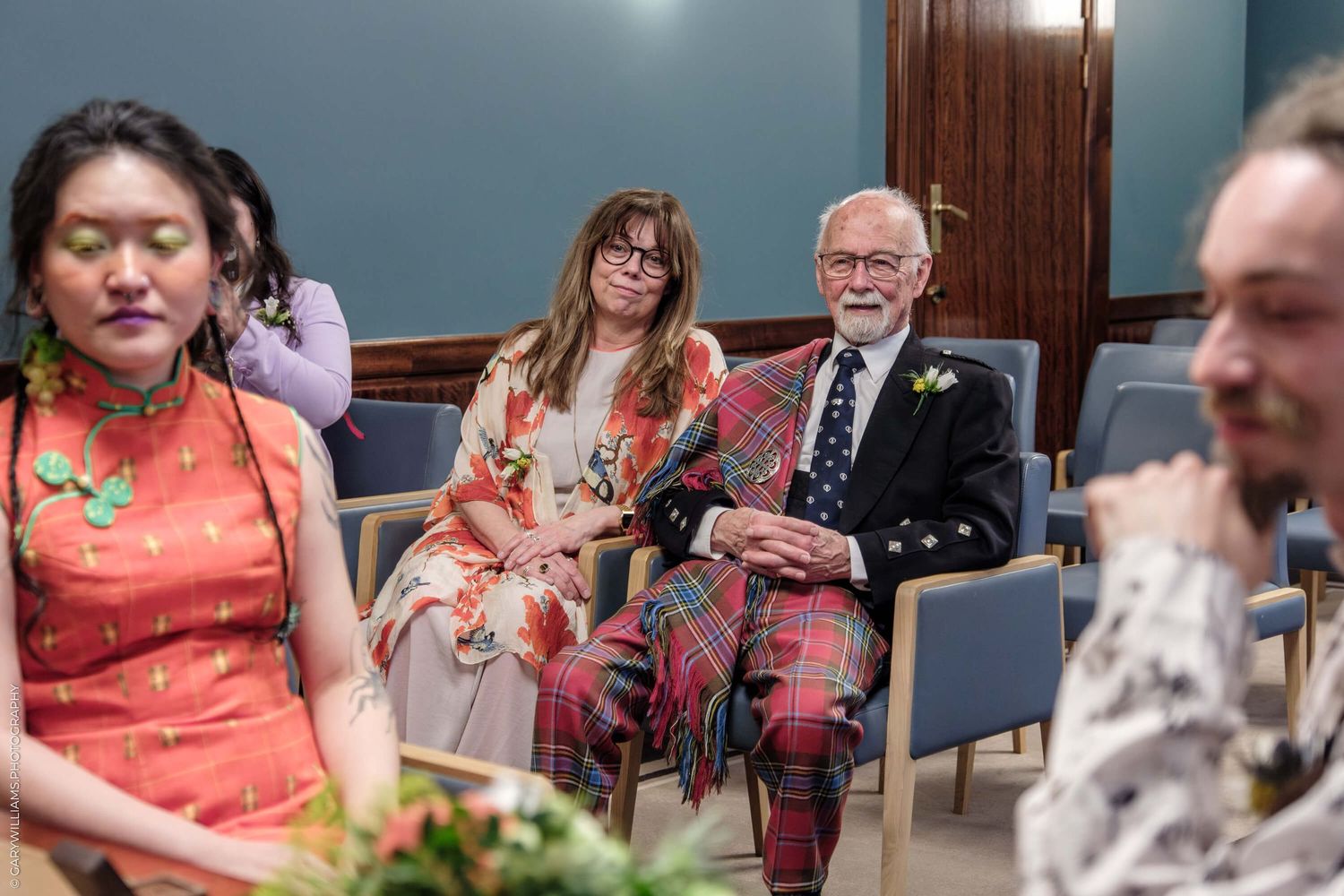 Wedding guests in coral and pink attire seated in rows at an intimate indoor ceremony.