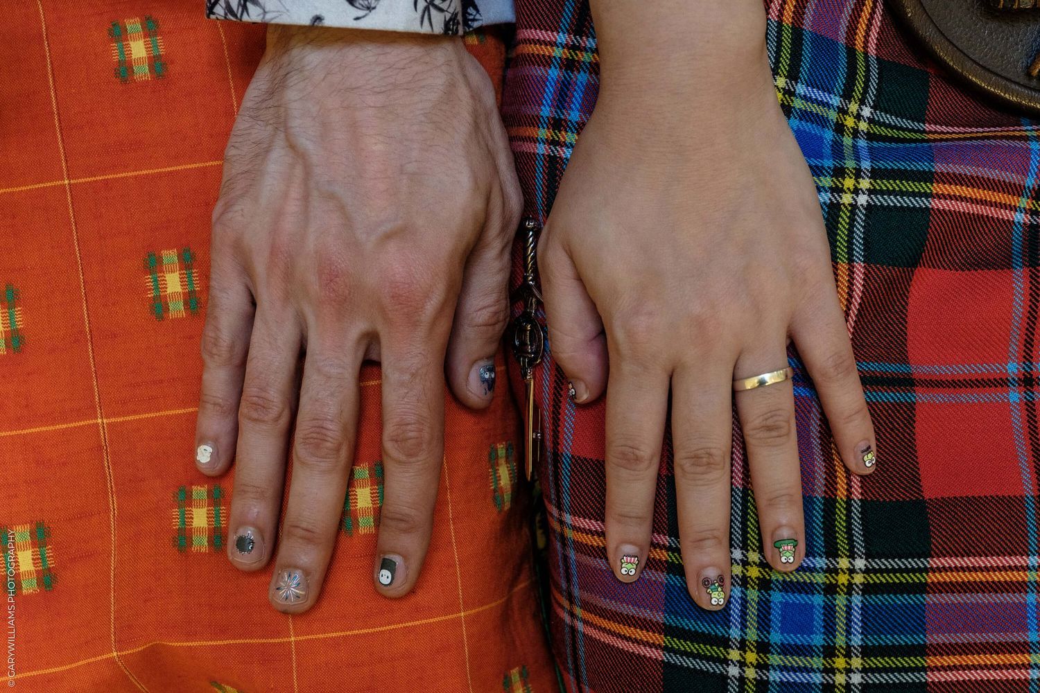Two hands wearing wedding rings rest on plaid fabric with a bright orange background.