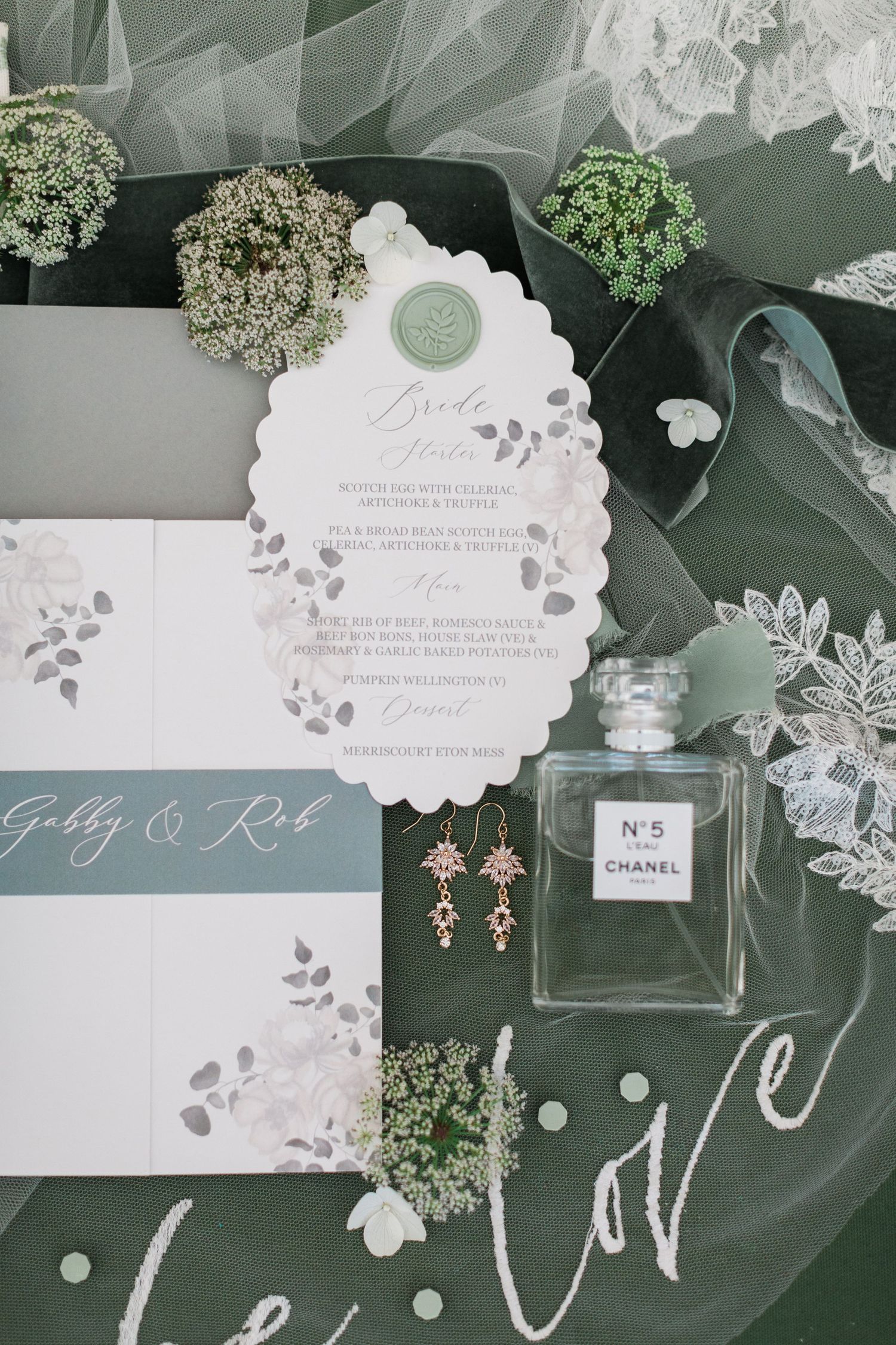 Elegant wedding flatlay featuring Chanel perfume, delicate earrings and white floral stationery with eucalyptus leaves by Hayley Elizabeth
