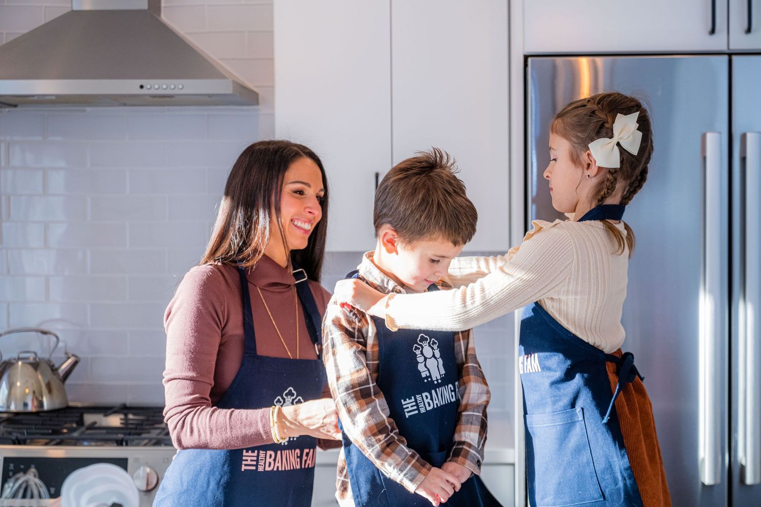 A group of people in aprons enjoy baking together in a bright modern kitchen with subway tile backsplash.