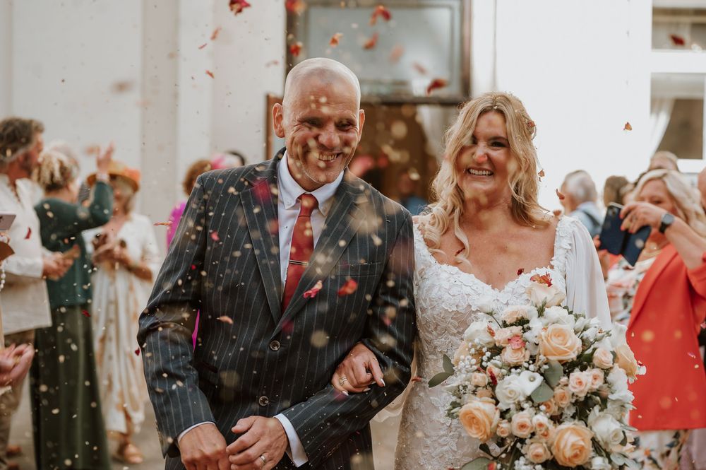 Smiling wedding celebration scene with confetti falling as happy couple celebrates with guests in formal attire.