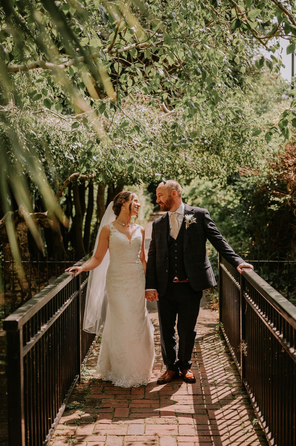 Newlyweds walking together on a brick bridge surrounded by lush greenery.