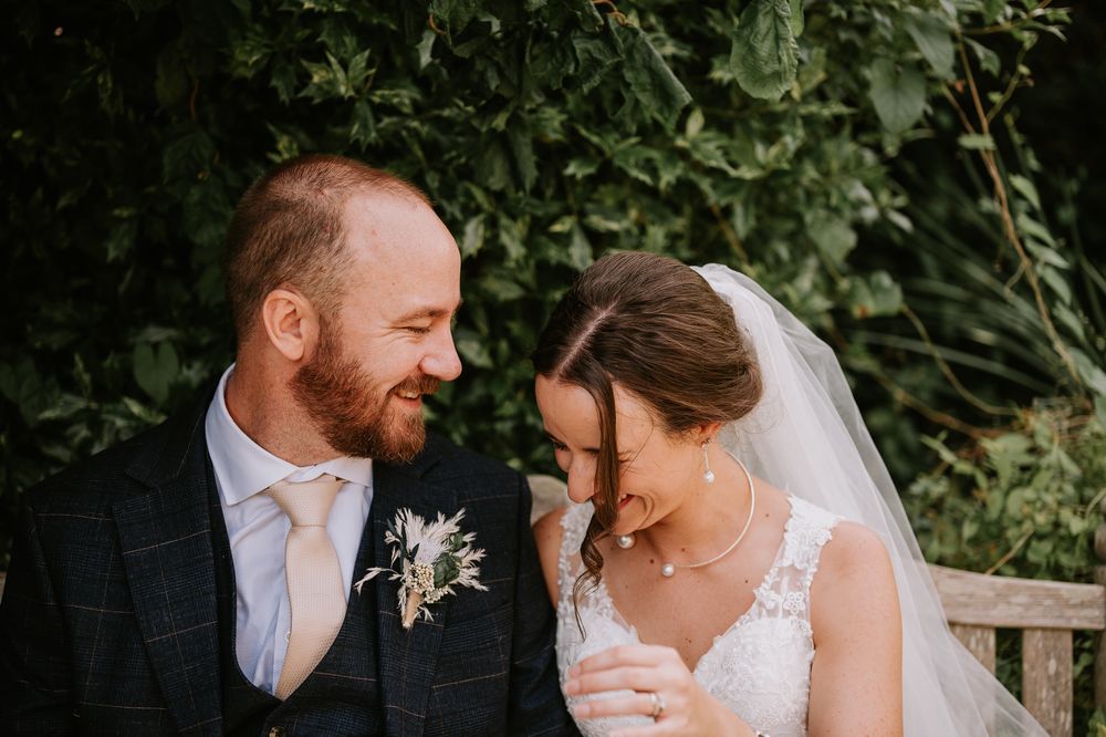 A bride and groom share joyful laughter and intimate moments in a garden wedding setting.