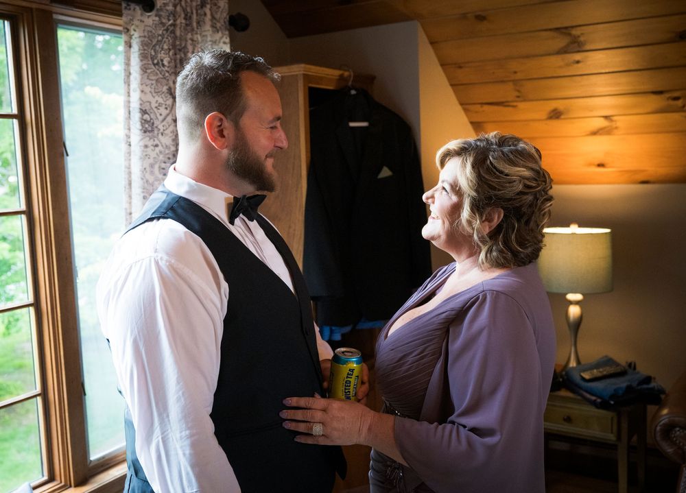 A tender moment between a parent helping with formal attire in a rustic wood-paneled room on wedding day.