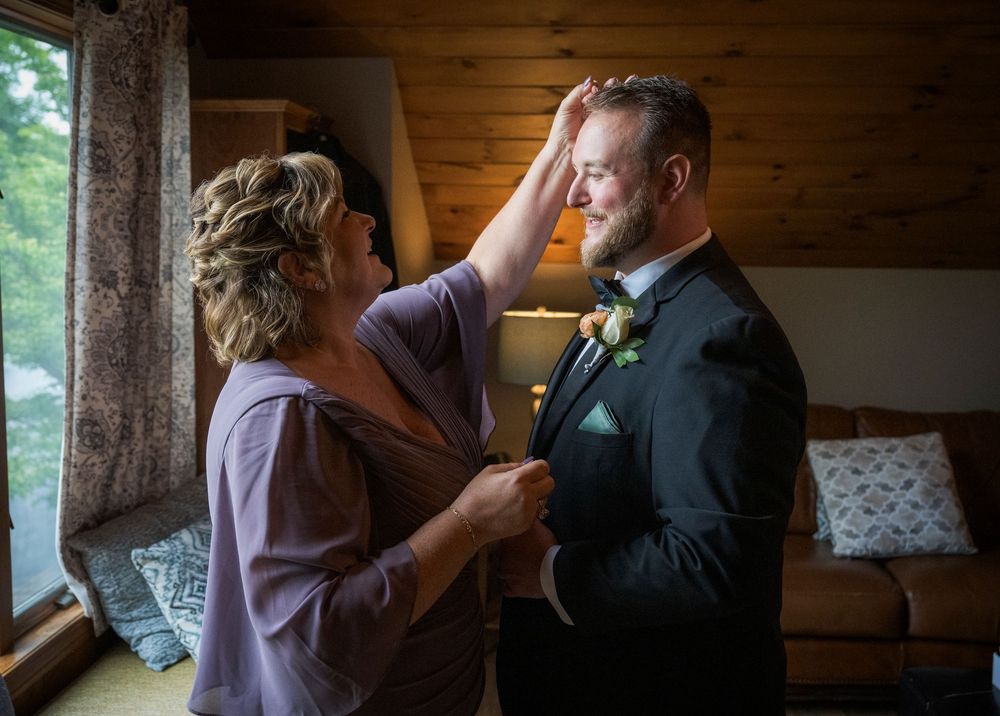 An intimate getting ready moment between parent and child on wedding day in front of a window.