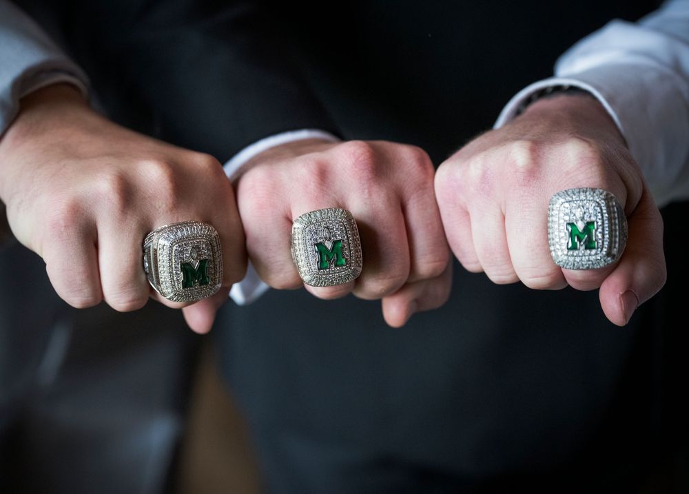 Three matching championship or class rings displayed on fingers against dark background.
