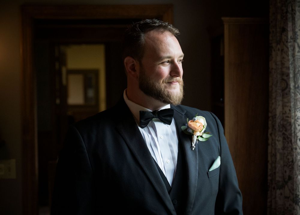 Formal portrait of person wearing black tuxedo with bowtie and boutonniere in dramatic lighting.