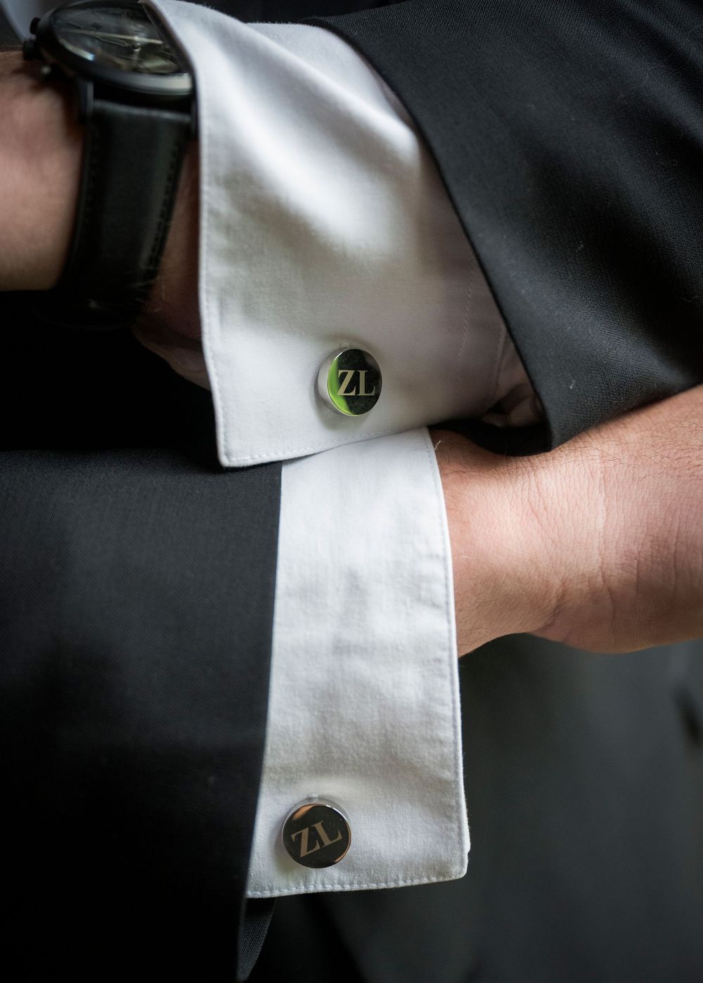 Close-up detail of green monogrammed cufflinks on white dress shirt cuffs.