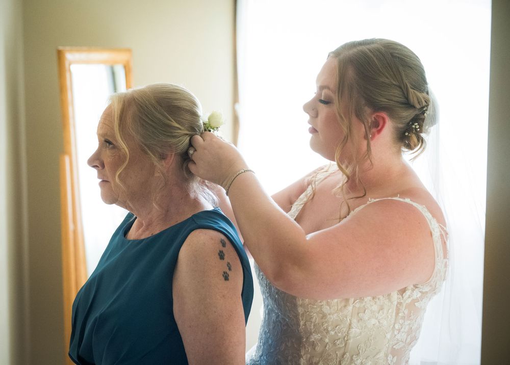 A tender getting ready moment between a person in a navy dress being helped with their hair.