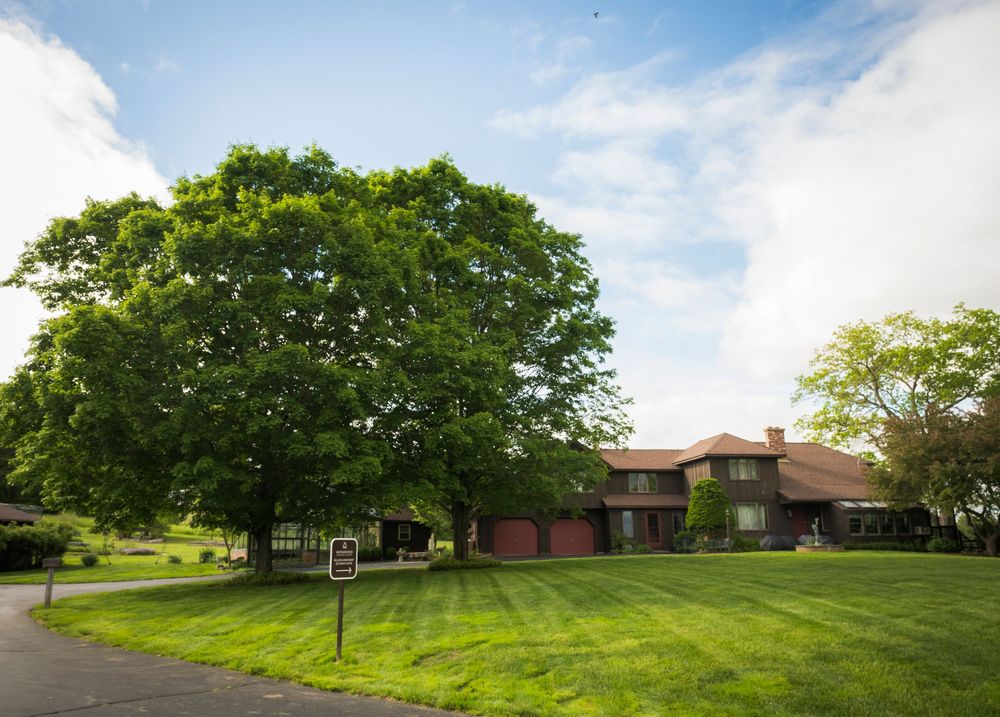 Brick building surrounded by lush green trees and manicured lawn on a sunny day.