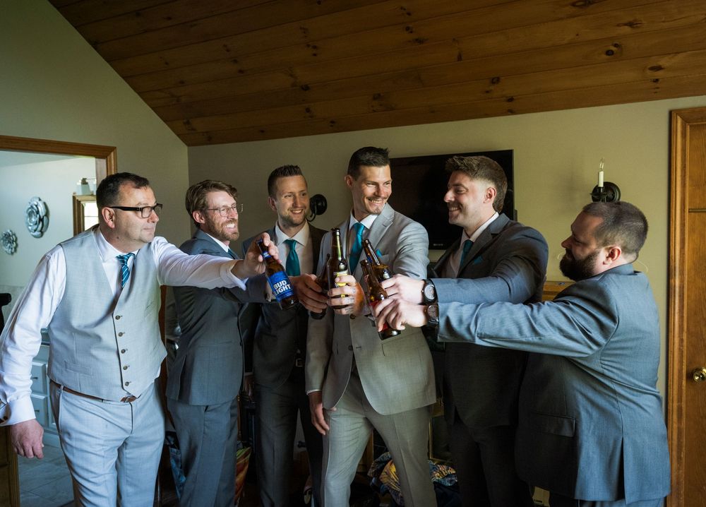 Groomsmen in suits toasting with drinks during wedding celebration.