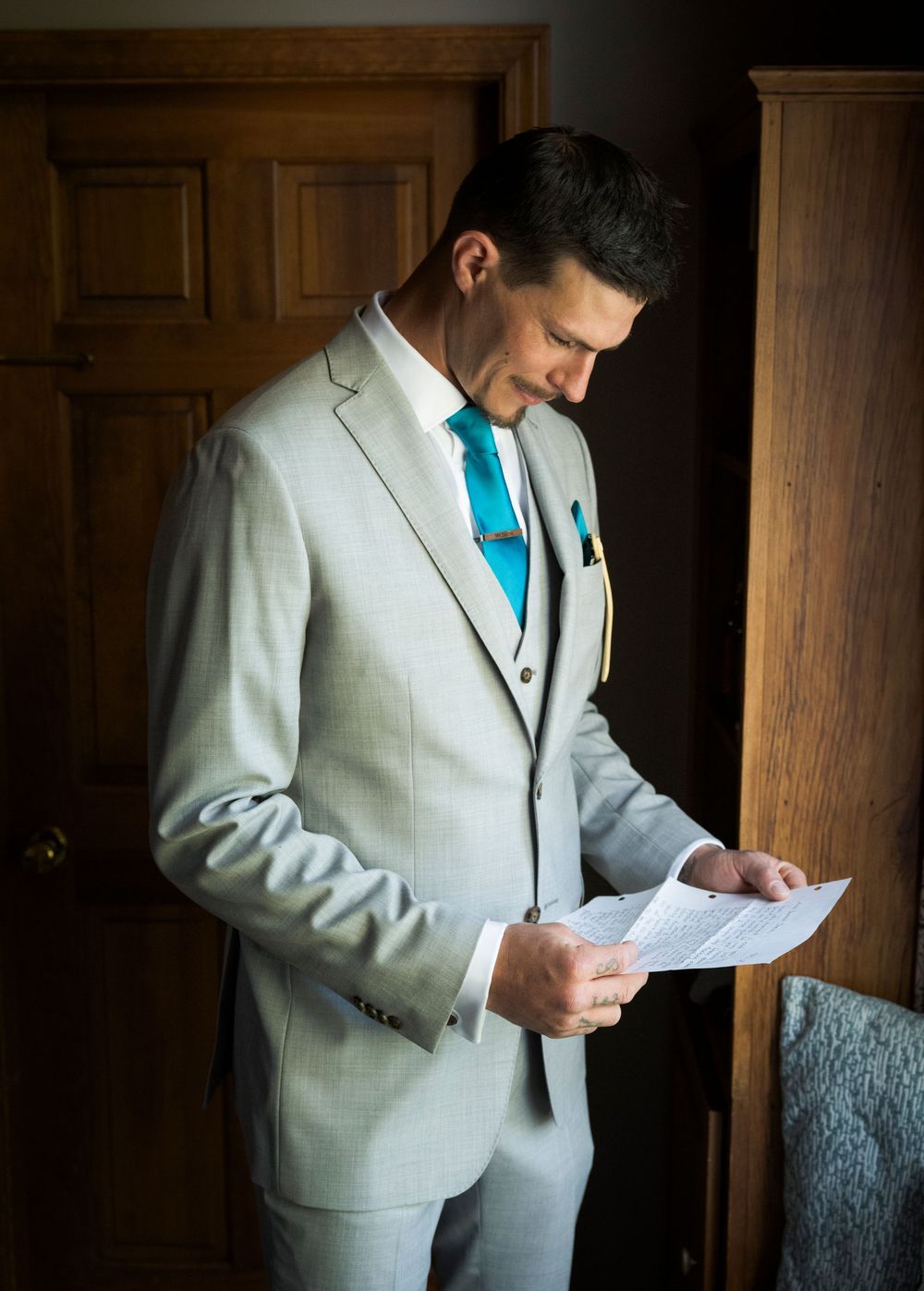 Groom in light gray suit with turquoise tie reading a letter before the ceremony.