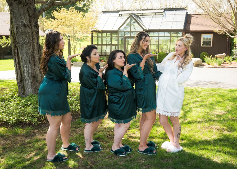A group in matching emerald green robes share a candid moment on a lawn near a greenhouse.