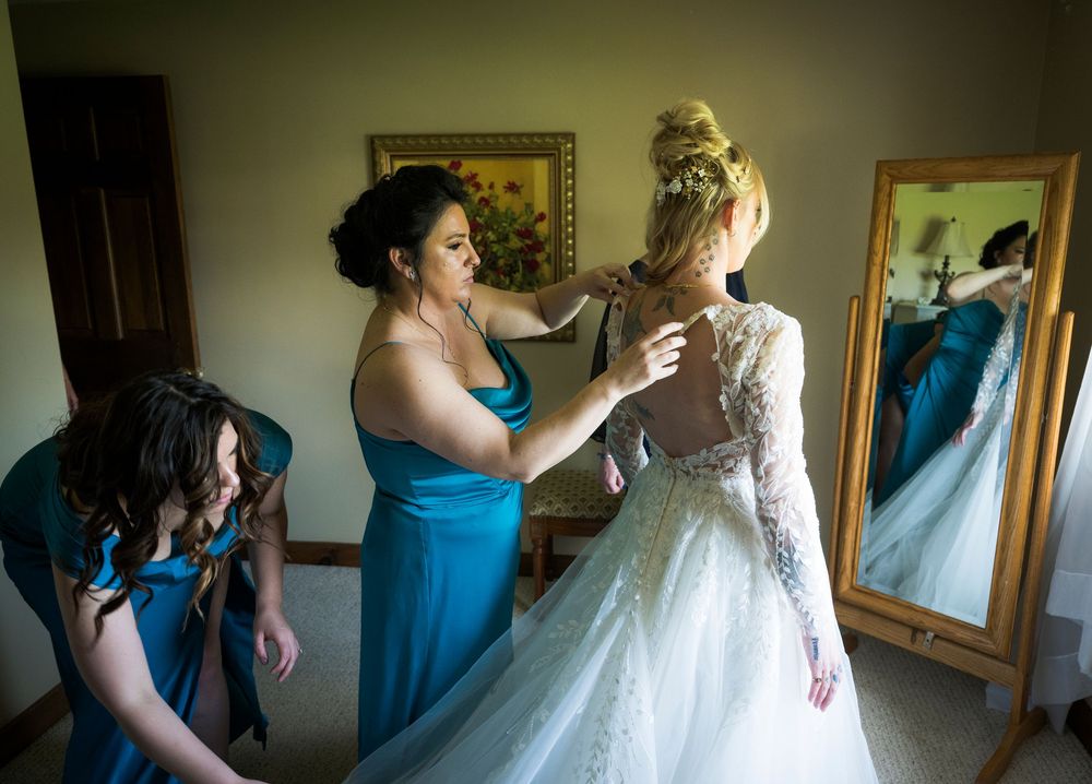 Wedding preparations show a bride getting final adjustments to her white lace gown while bridesmaids in blue dresses assist.