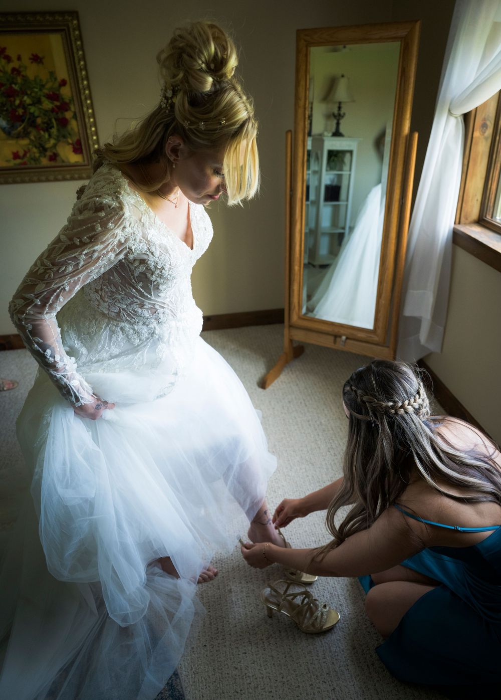 A wedding dress being adjusted in a room with mirrors and floral artwork.