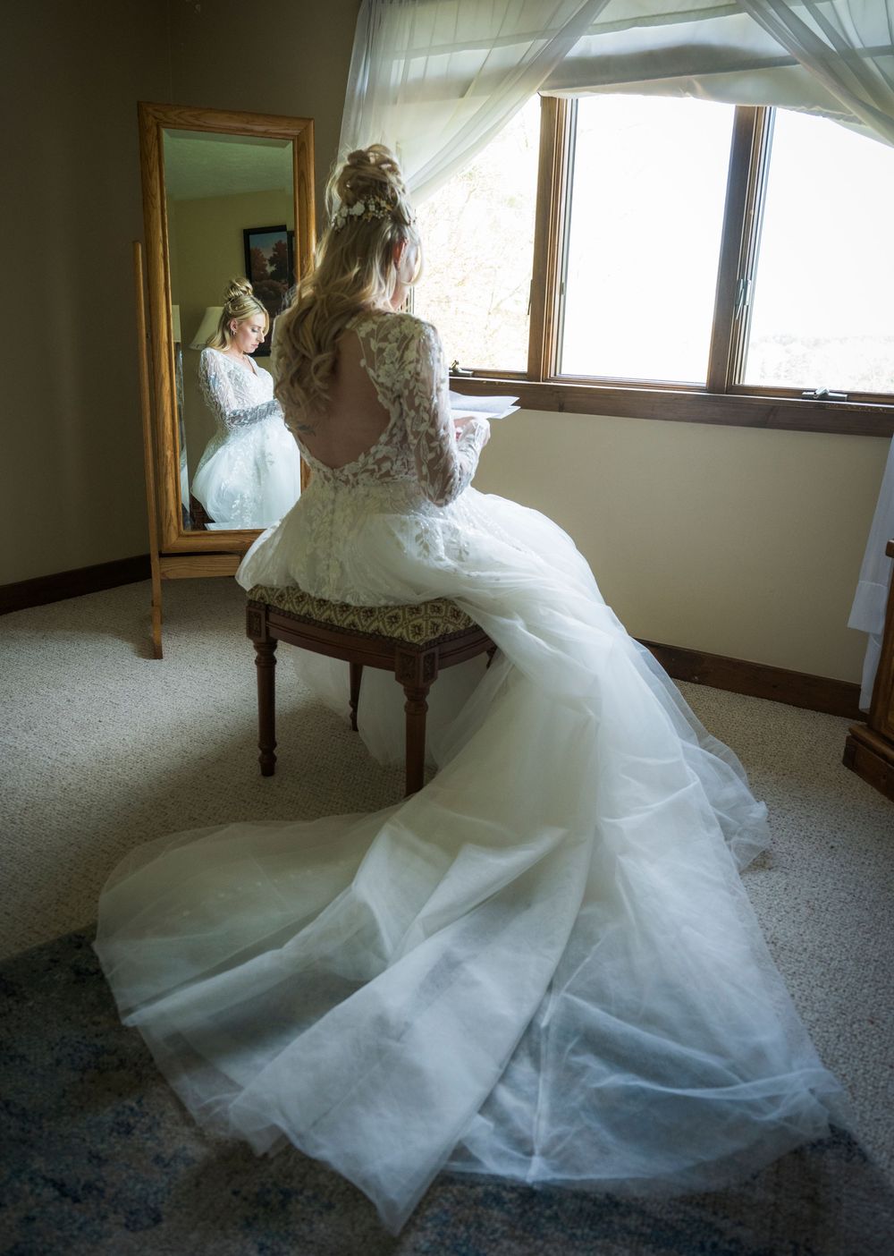 An elegant lace wedding gown with flowing train captured in reflection of a full-length mirror.