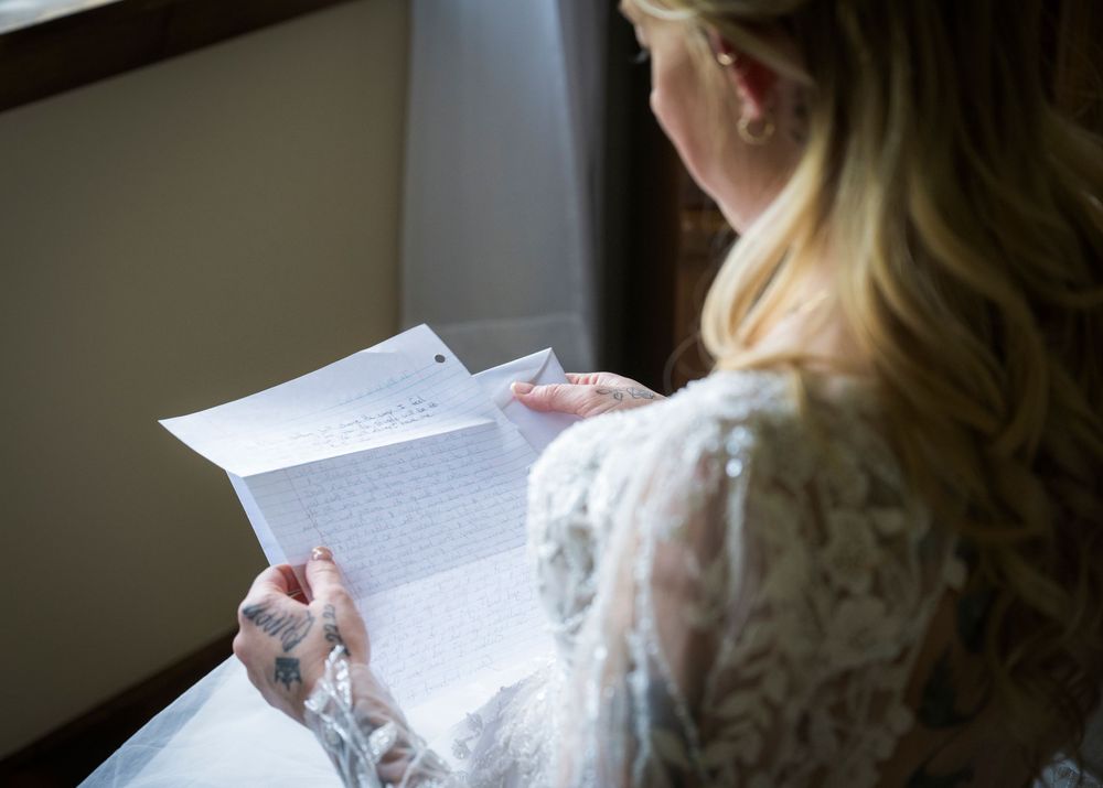 Someone in a white lace dress reads a letter by window light creating a soft atmospheric scene.