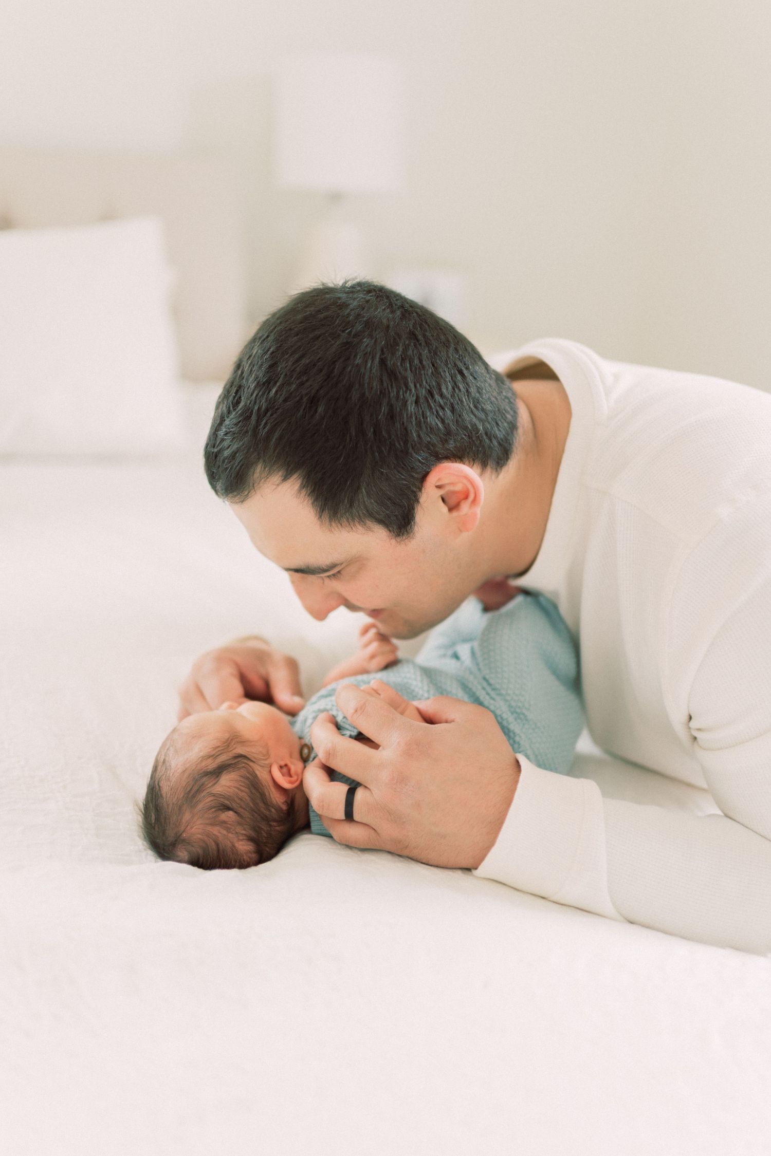 A tender moment between a parent and tiny newborn baby on a white bed.