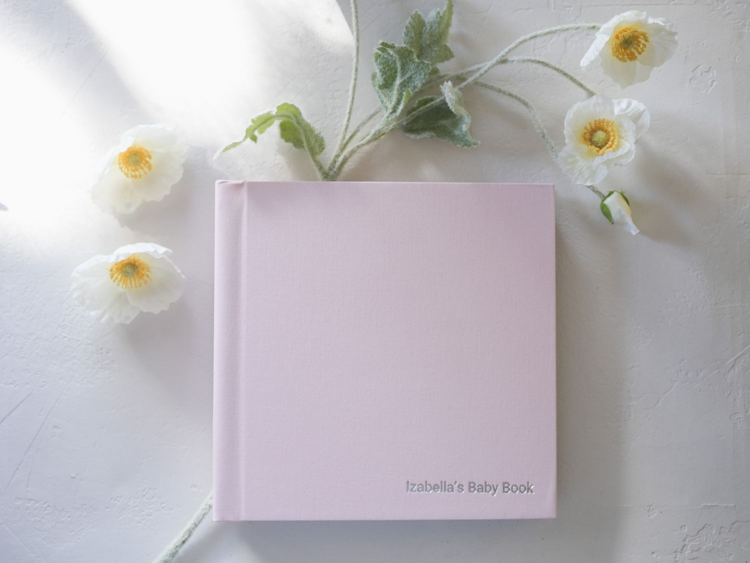 Soft pink baby photo album cover with white flowers scattered around the edges.