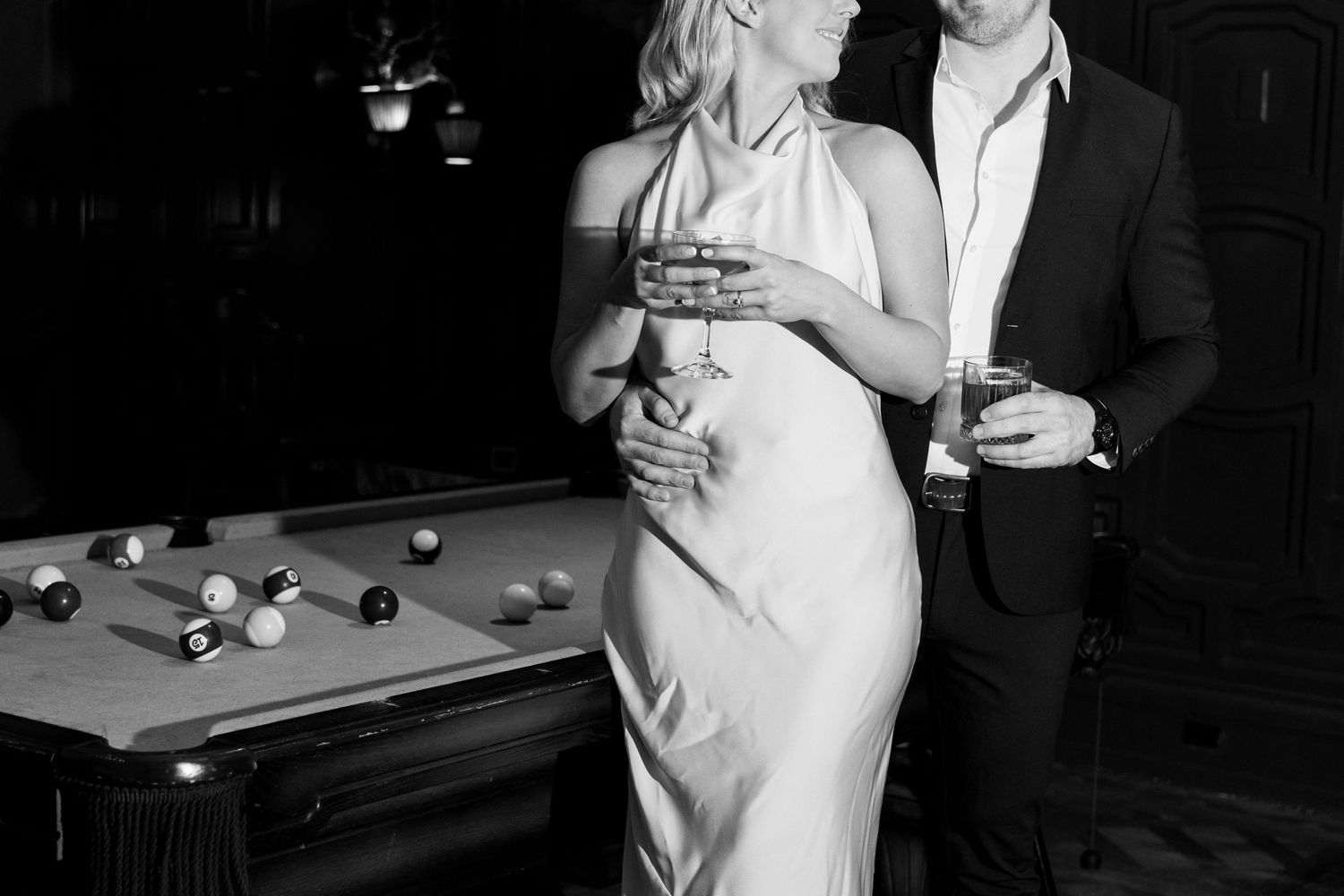 A couple sharing drinks beside a pool table in an intimate bar setting. Engagement Session at The Lafayette Hotel in San Diego. JPPC