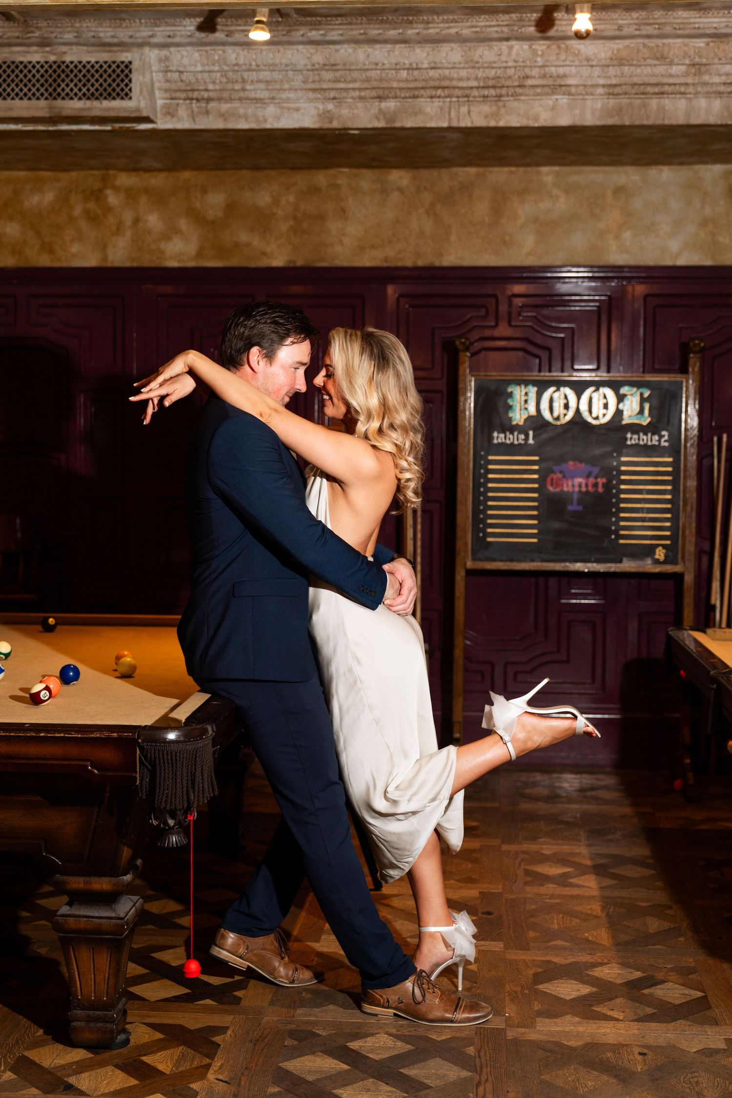 Couple dancing romantically in vintage bar setting with pool table and wood paneling. Engagement Session at The Lafayette Hotel in San Diego