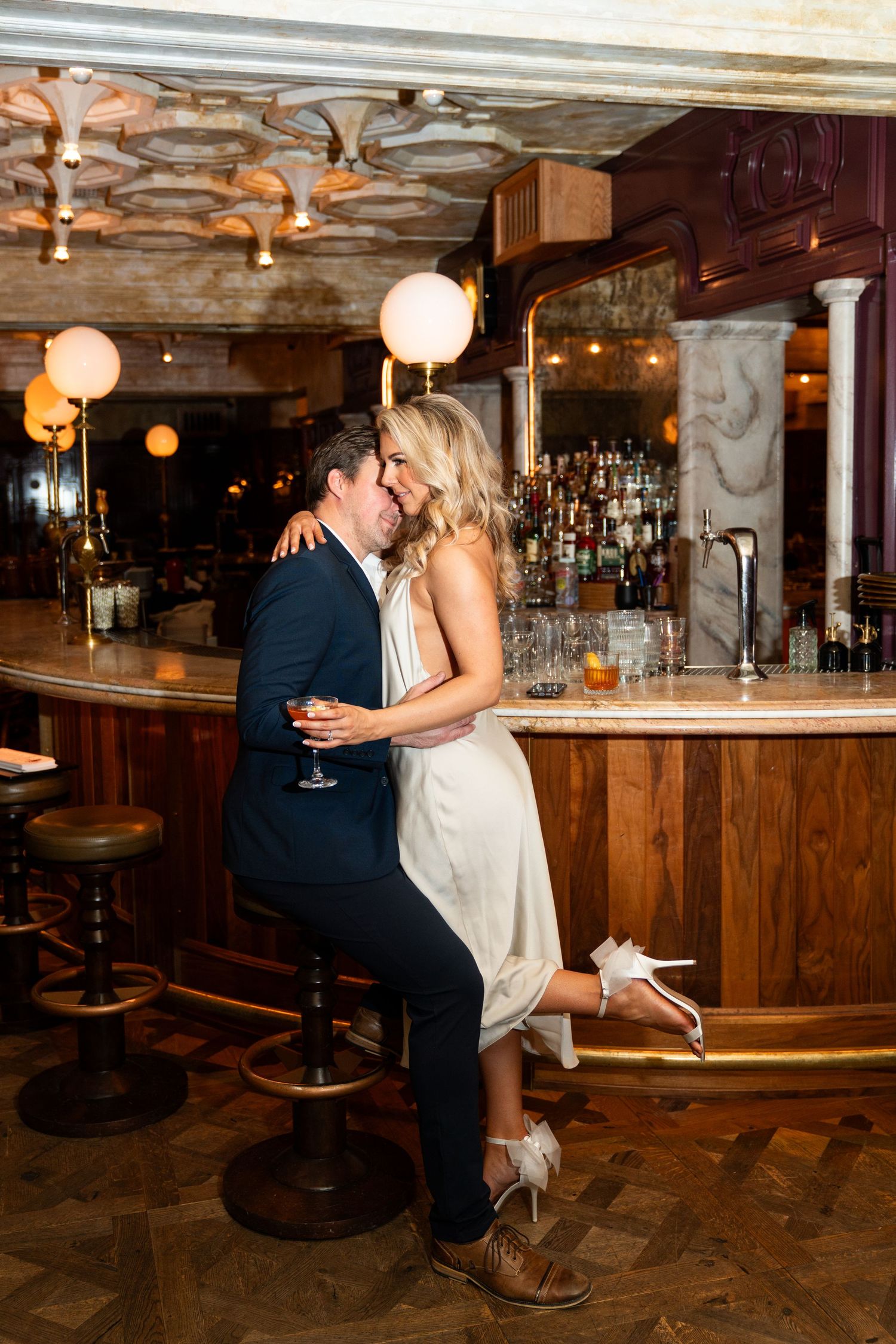 Intimate moment at curved wooden bar with globe lights and vintage decor. Engagement Session at The Lafayette Hotel in San Diego. JPPC