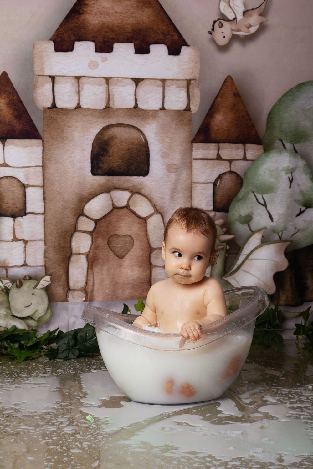 Small child taking milk bath in glass bowl with fairy tale castle background and soft lighting.