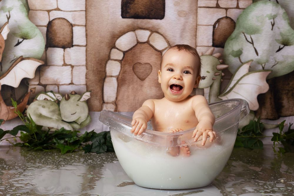 A joyful small child sits in a white bowl against a fantasy castle backdrop with floral decorations.