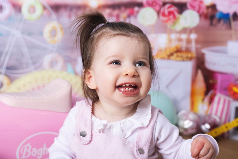 A happy child in a pink outfit smiles joyfully while playing with toys in a colorful, pastel-themed setting.