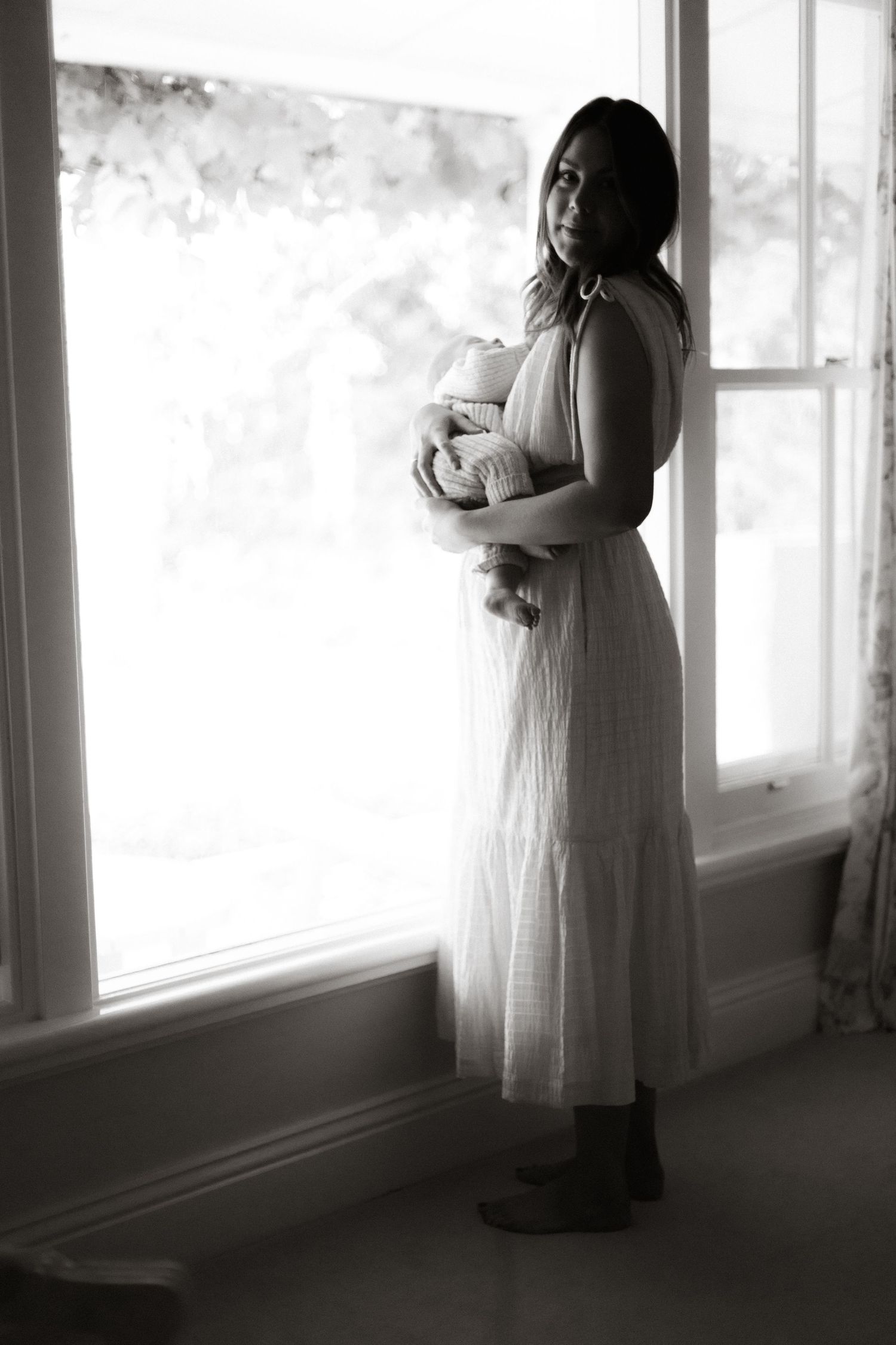 Mother rocking her newborn looking out of her home window