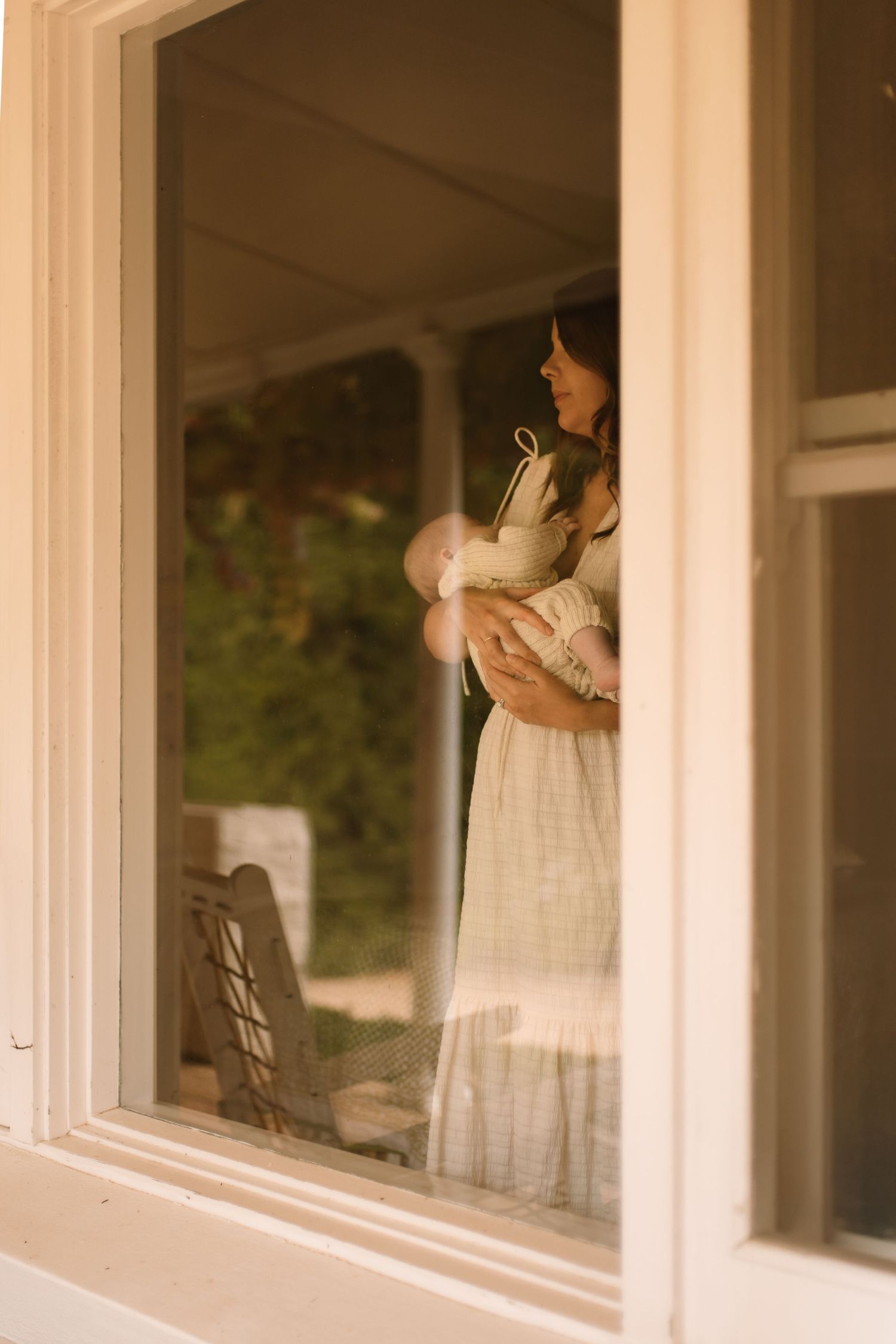 Mother rocking her newborn looking out of her home window