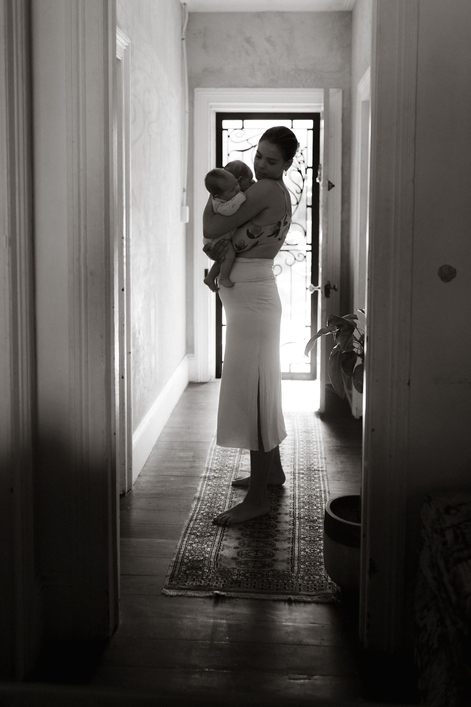Storytelling photography session of mother and her newborn twins, standing in the light of their doorway