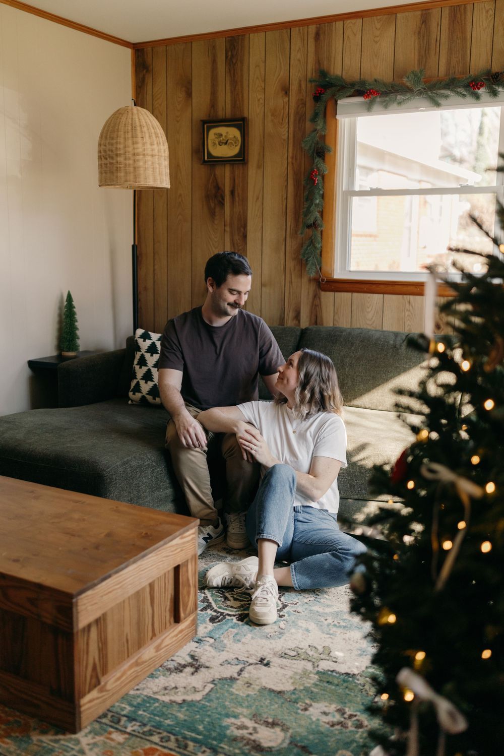 Couple relaxing on couch near Christmas tree in rustic wood-paneled living room.