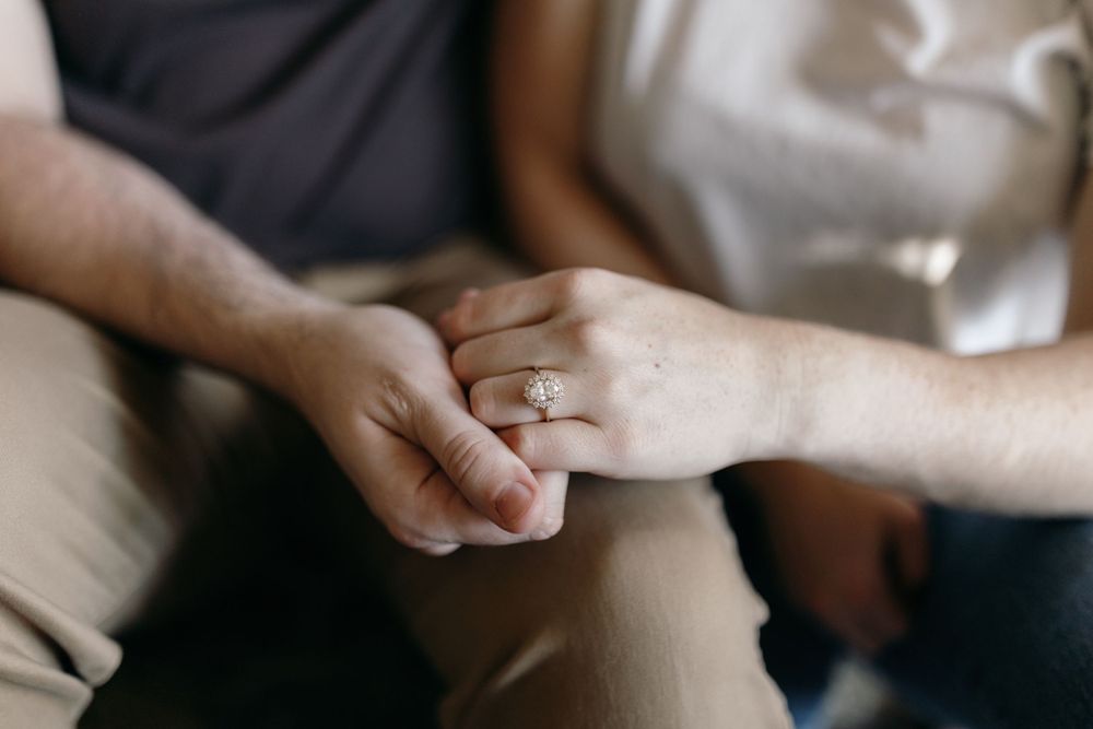 Close-up shot of hands tenderly holding each other against neutral background.