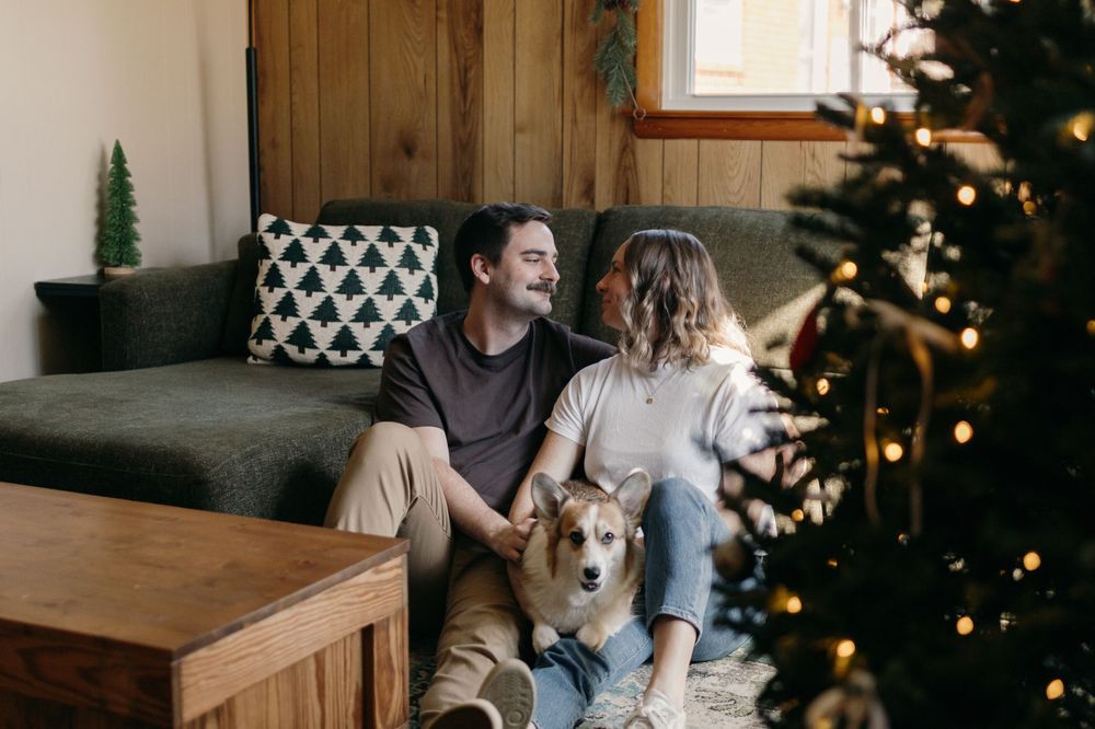 Couple sitting on couch with their Corgi dog next to decorated Christmas tree.