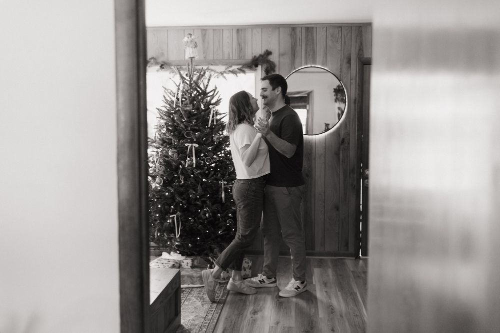 Black and white image of couple decorating Christmas tree together.