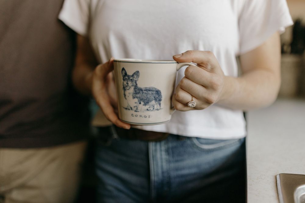 Hands holding a coffee mug with a dog illustration in a rustic kitchen setting.