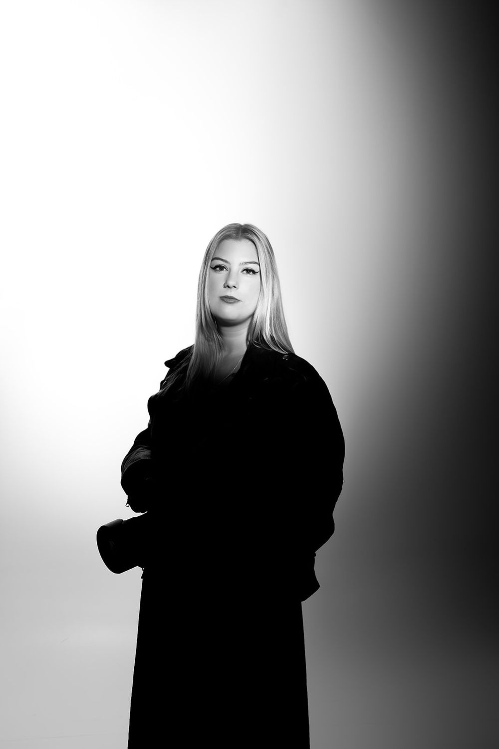 Black and white portrait of a person in a dark winter coat looking upward against a gradient studio background.