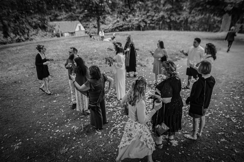 Wedding guests gather on a grassy lawn for an outdoor celebration with natural surroundings in black and white.