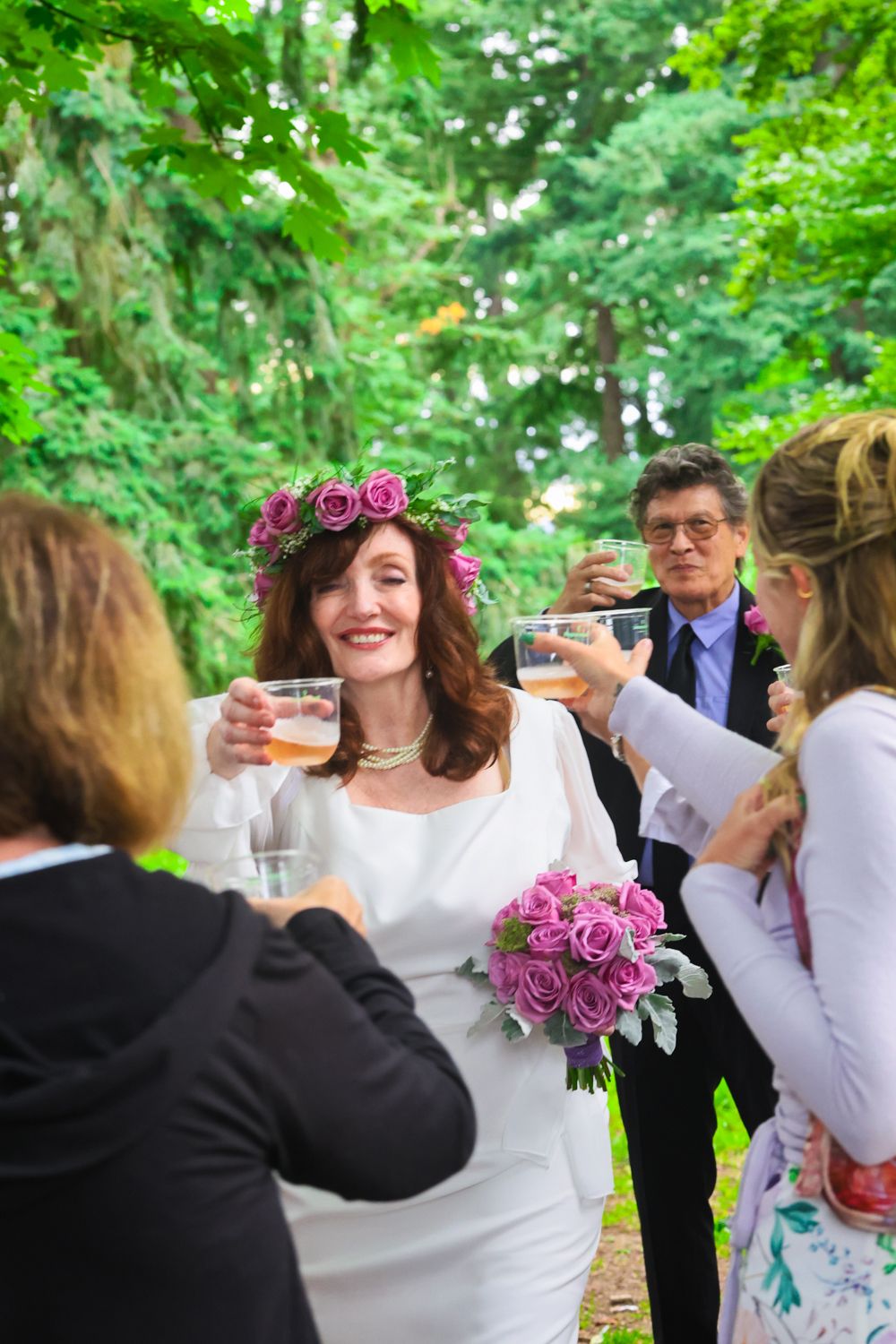 Wedding guests celebrate with toasts in an outdoor garden setting with pink floral decor and bouquet.